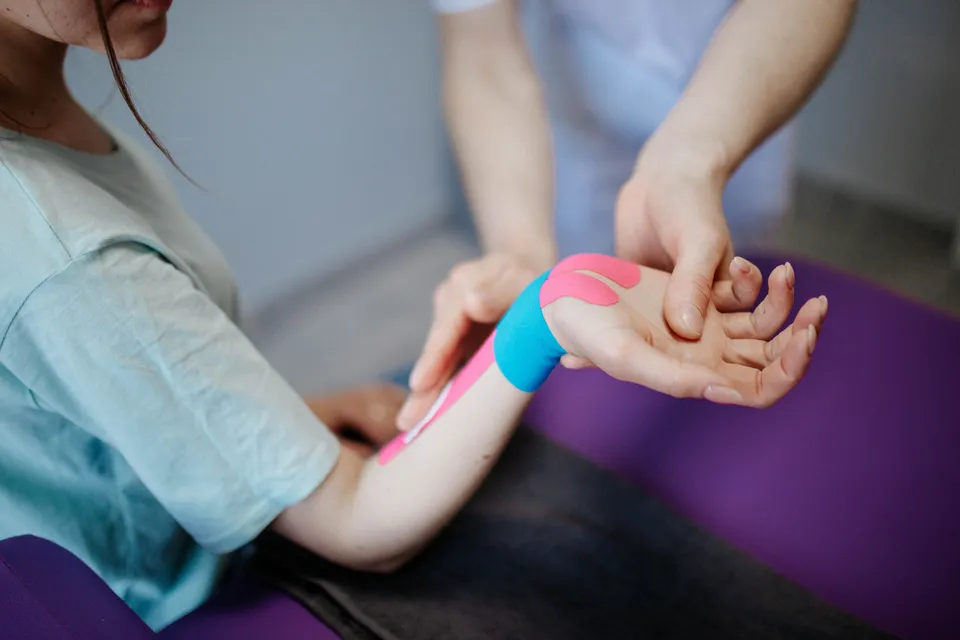 Fisioterapeuta aplicando vendaje neuromuscular de colores en el antebrazo de una paciente