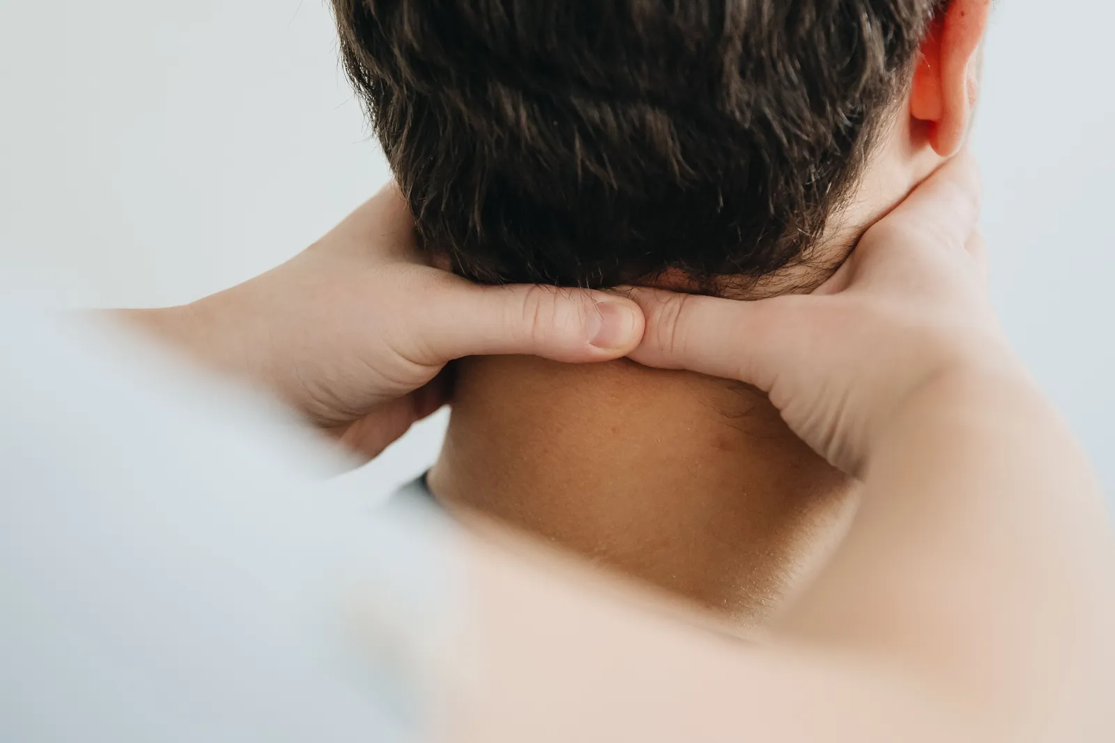 Manos de fisioterapeuta presionando con los pulgares la nuca y la base del cuello de una persona vista de espaldas
